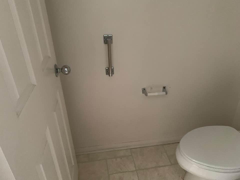 A small bathroom featuring a toilet, grab bar, and toilet paper holder.