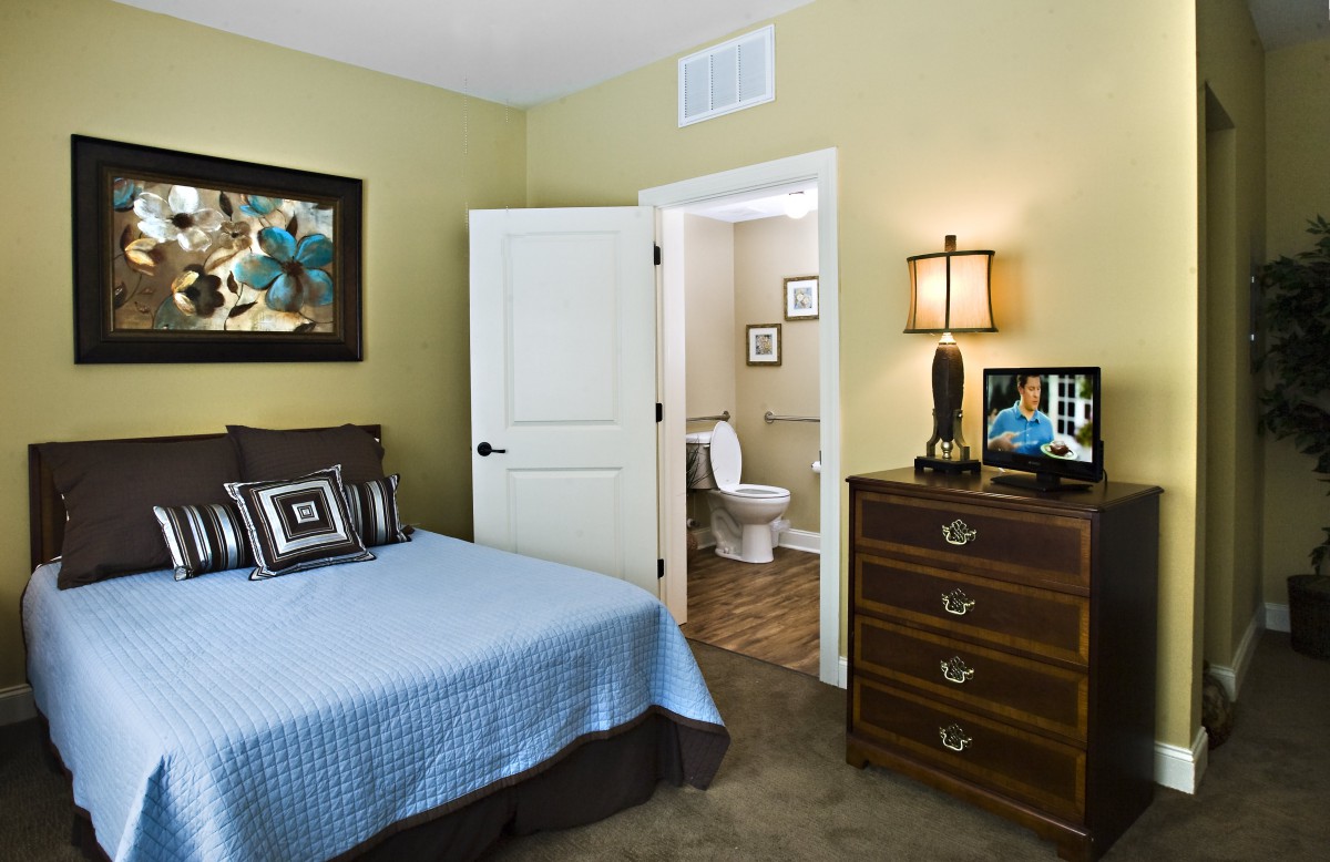A cozy bedroom with a blue bedspread, wooden dresser, and an open door leading to a bathroom.