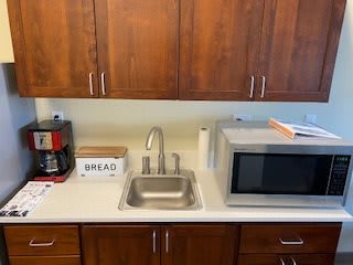 A kitchen countertop with a sink, coffee maker, bread box, and microwave.