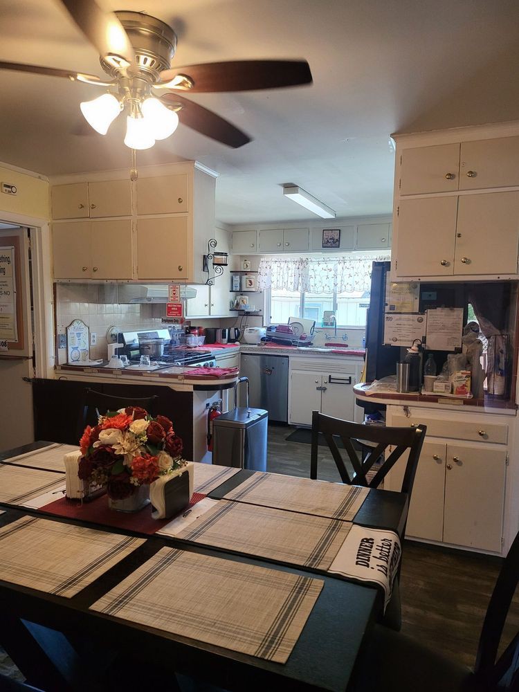 A cozy kitchen with a dining area, featuring white cabinets, a ceiling fan, and various appliances.