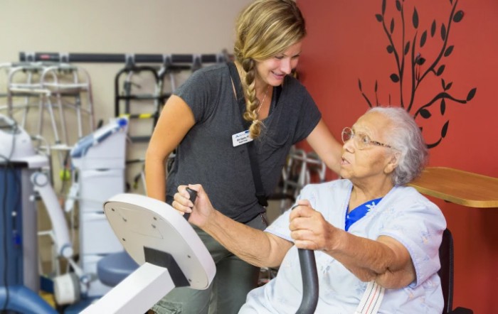 A healthcare professional assists an elderly person during a rehabilitation exercise session.