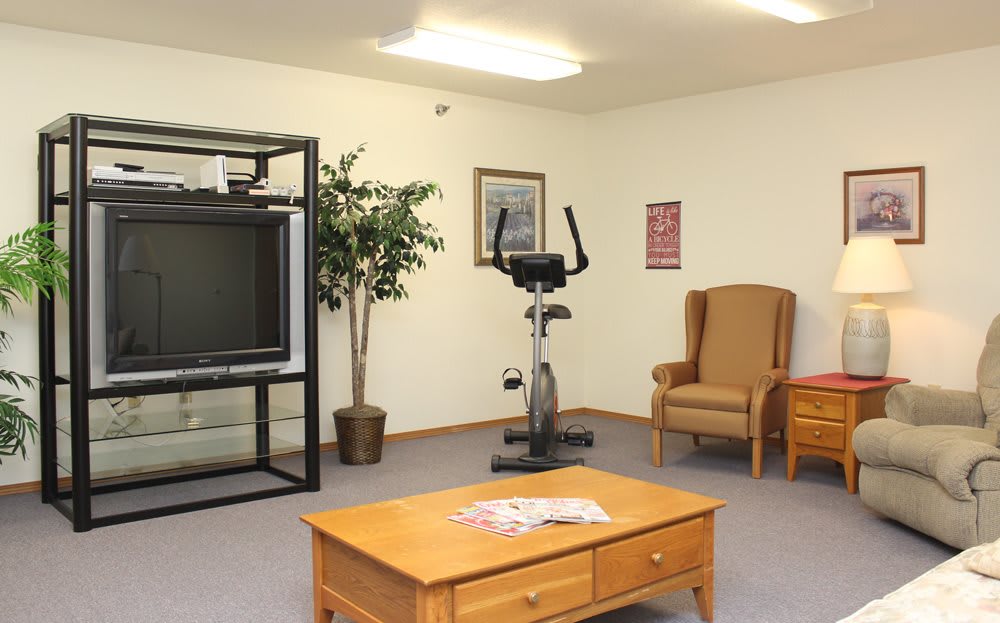 A living room with an exercise bike, TV, coffee table, and armchair arranged neatly.
