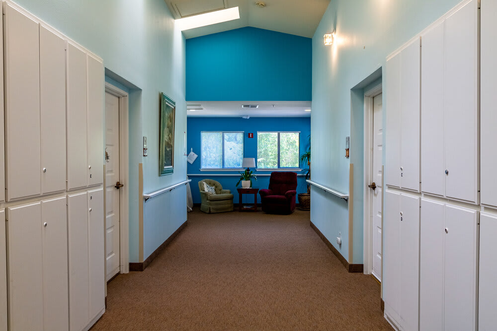 A well-lit hallway with blue walls leading to a seating area with two chairs by the window.
