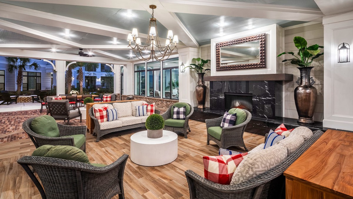 A cozy living room with comfortable seating around a fireplace, accented by plaid pillows and a chandelier.