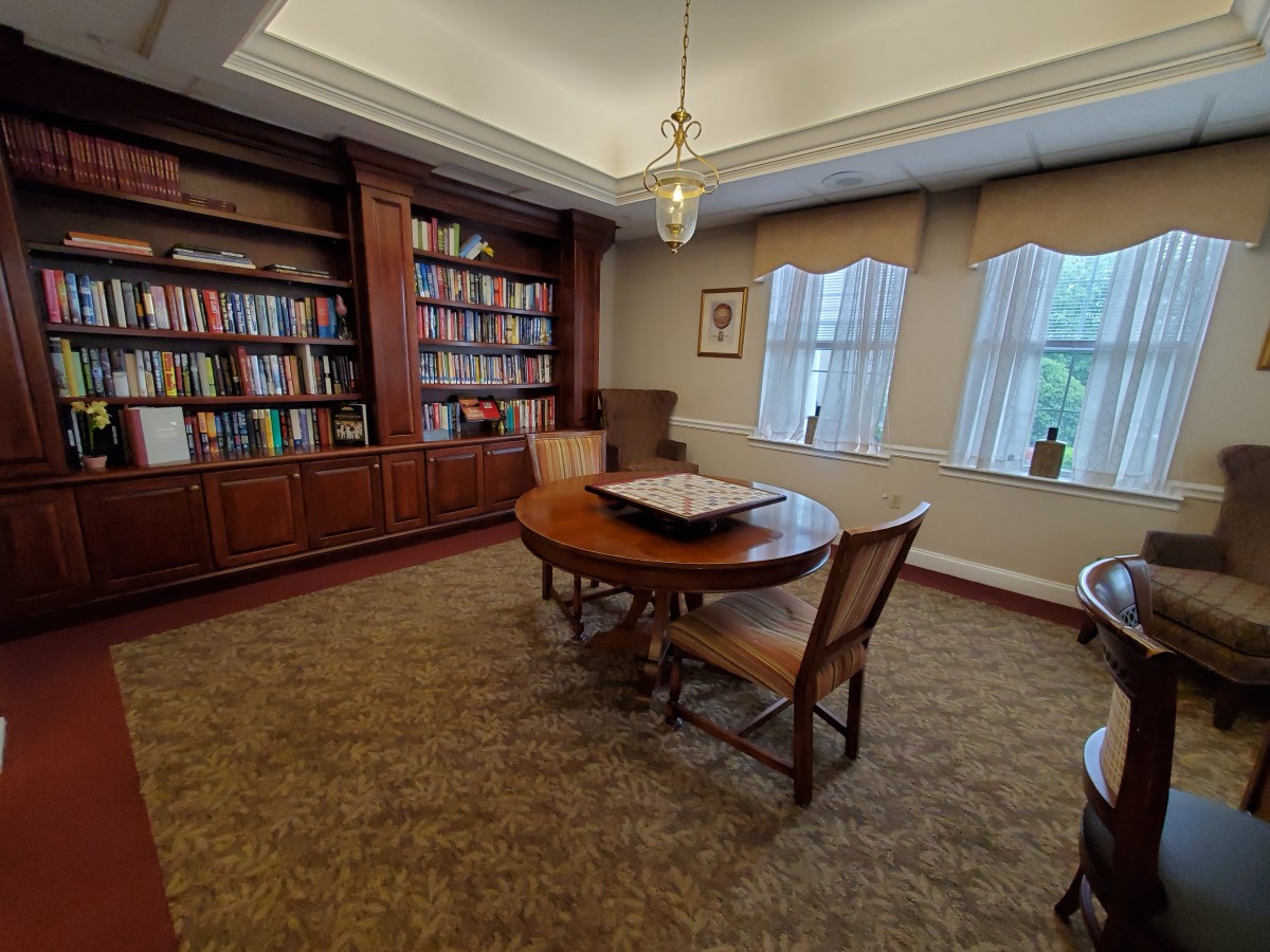 A cozy library room with bookshelves, a round table, and chairs near large windows.