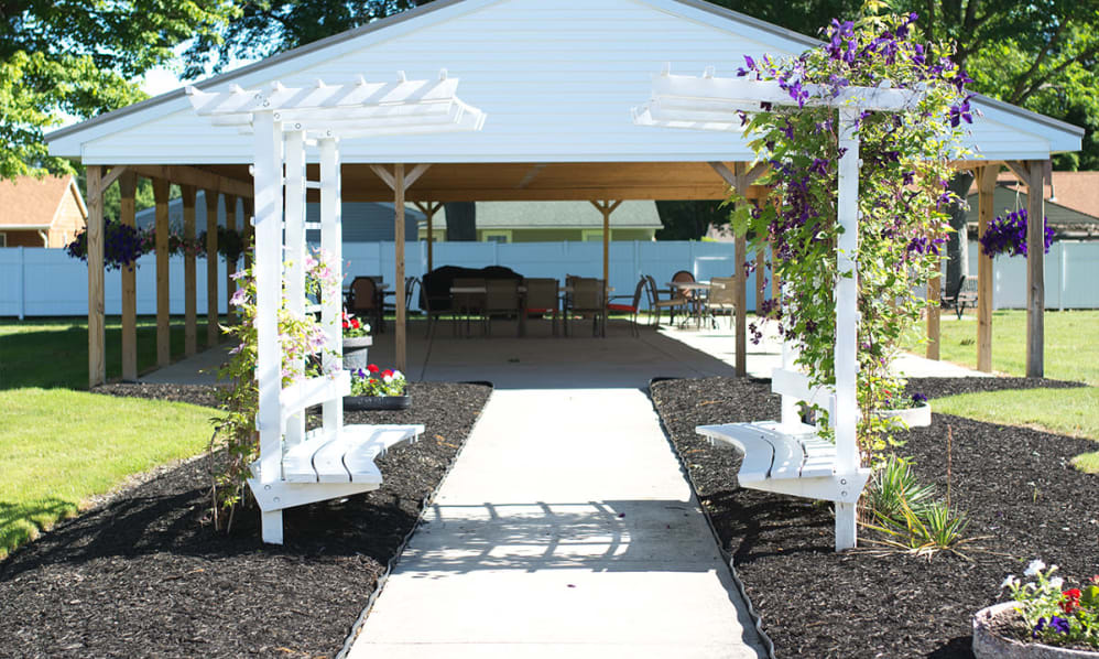 A charming pergola with benches and flowers lines a pathway leading to an outdoor seating area.