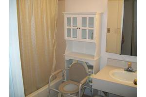 A bathroom featuring a storage cabinet, sink, shower curtain, and commode chair.