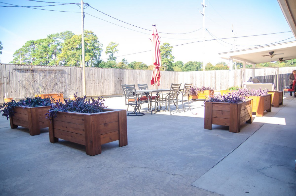 A sunny outdoor patio with furniture, including tables, chairs, planters, and an umbrella.
