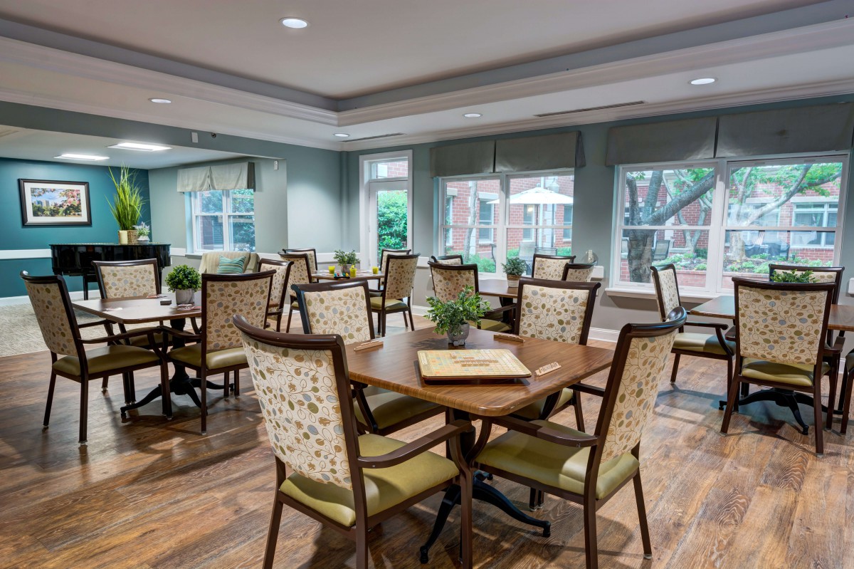A spacious and elegantly designed dining room with multiple tables and chairs, featuring large windows and decorative plants.