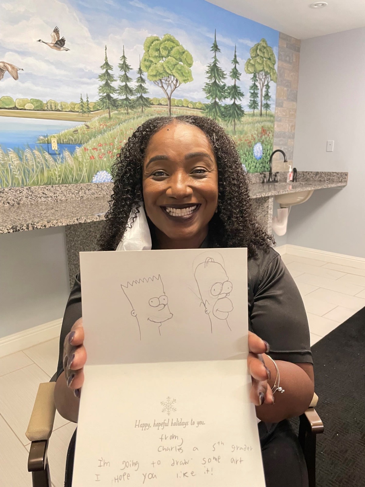 A person smiling while holding an open card with artwork in a room.