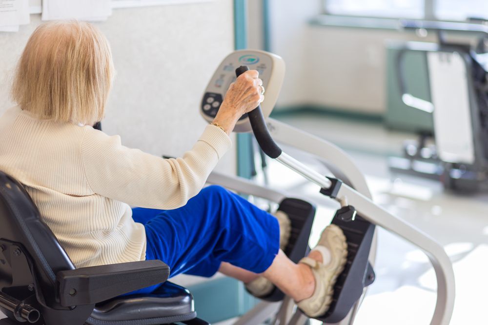 An elderly person using an exercise machine indoors for physical therapy.