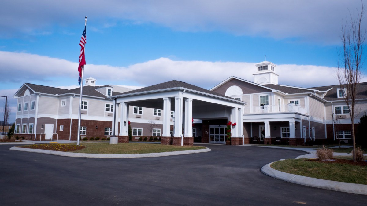 A modern hospital building with an American flag and a spacious driveway under a cloudy sky.