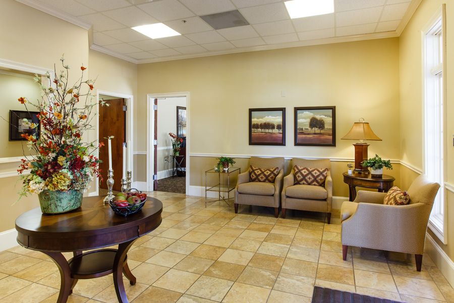A cozy waiting room with plush seating, decorative plants, and framed artwork on the walls.