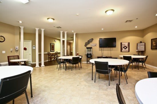 A spacious and well-lit conference room with round tables and chairs, featuring a mounted television on the wall.