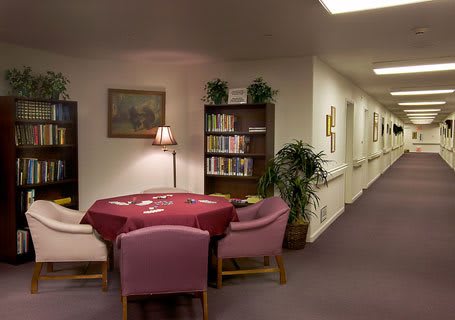 A cozy reading nook with a round table and chairs, surrounded by bookshelves in a quiet corridor.