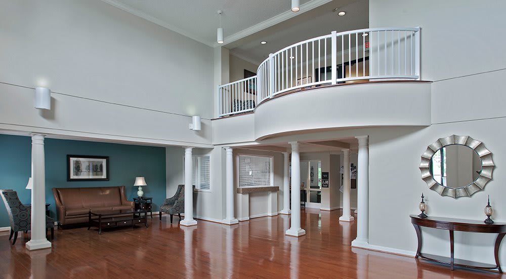 A modern living room with a high ceiling, featuring a balcony, columns, and hardwood flooring.