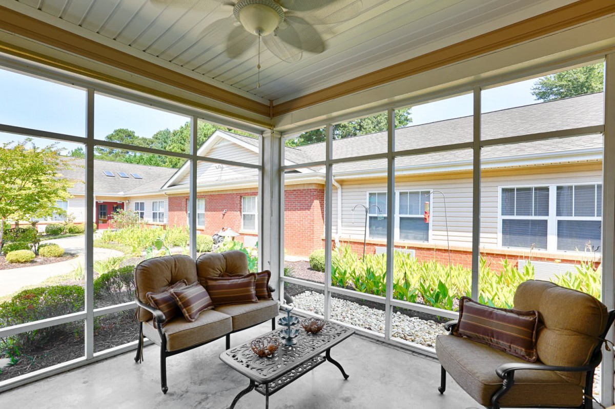 A cozy sunroom with comfortable seating and a ceiling fan, offering views of the outdoors.
