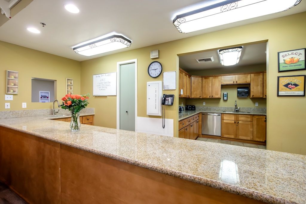 A well-lit office reception area with a counter, flowers, and a view into a small kitchen.
