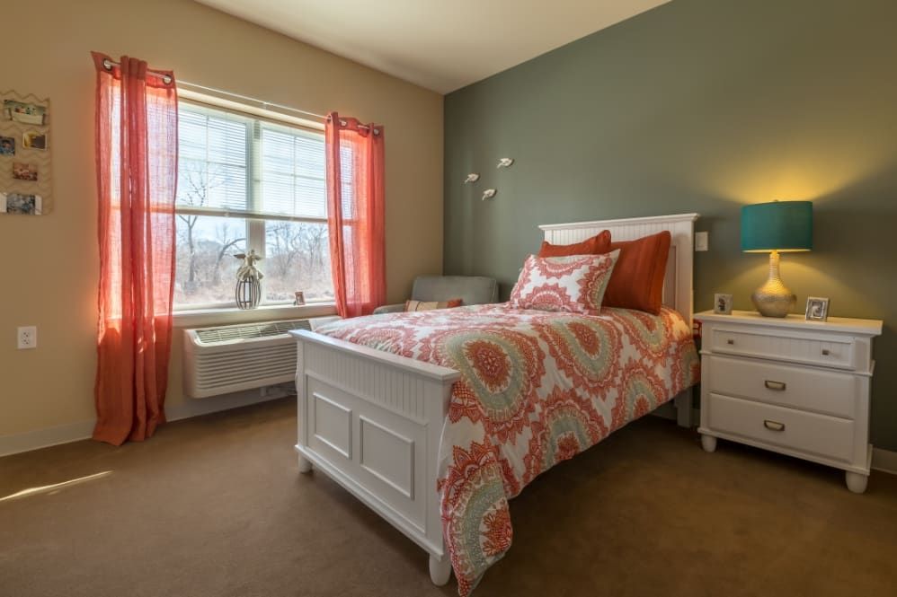 A cozy bedroom with a single bed, colorful bedding, and a well-lit window.