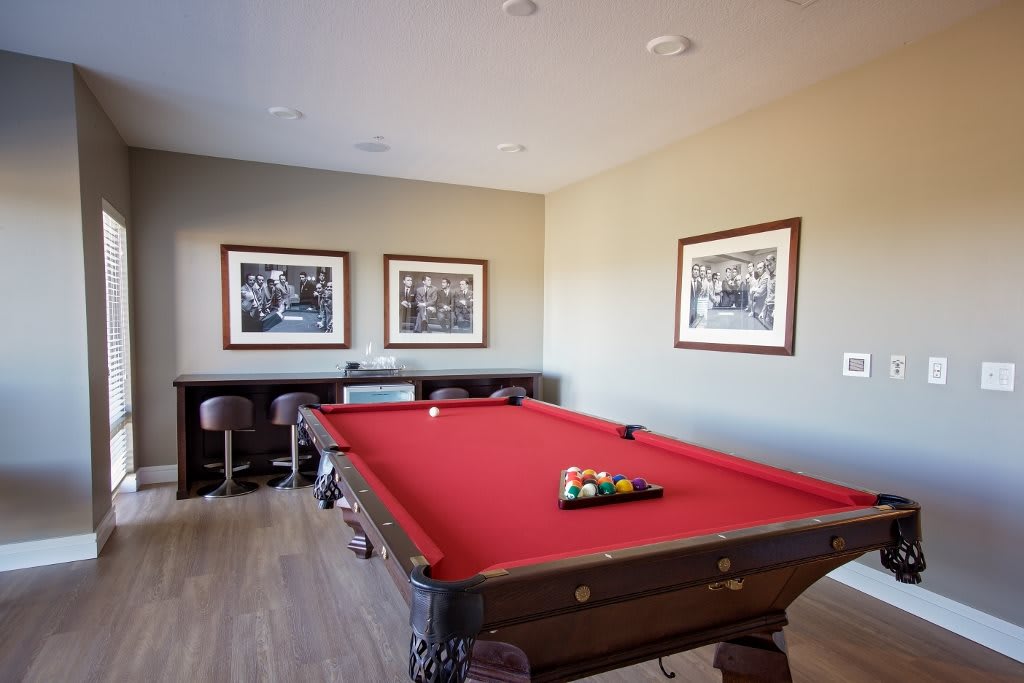 A modern billiards room with a red-felt pool table and bar stools against the wall, decorated with framed pictures.