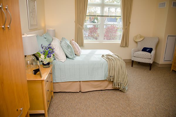 A cozy bedroom with a neatly made bed, soft decor, and a window bringing in natural light.