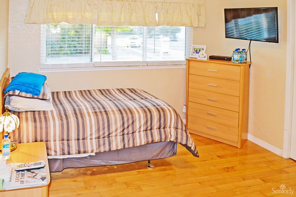 A cozy bedroom with a striped bedspread, wooden dresser, and large window.