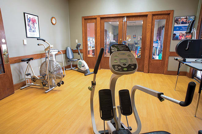 A fitness room equipped with various exercise machines, including an elliptical, treadmill, and stationary bike.
