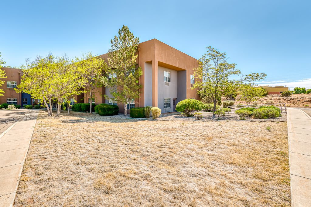 A modern house set in a desert landscape with sparse trees under a clear blue sky.