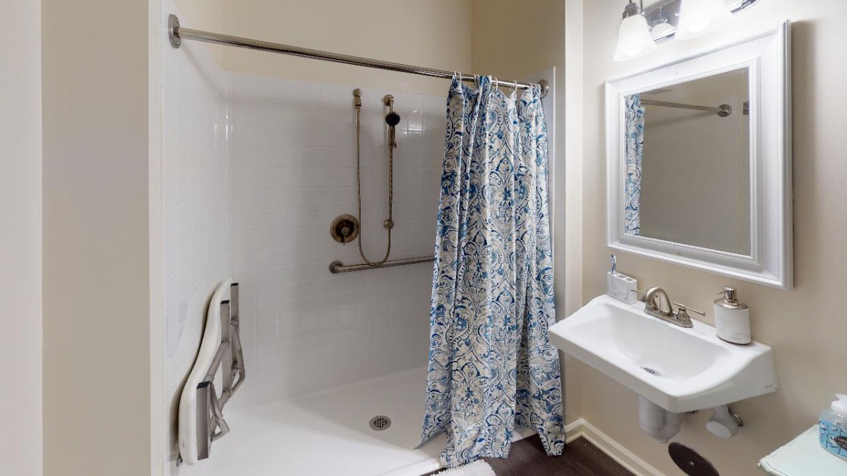 A bathroom featuring a shower with a floral curtain, grab bar, and a pedestal sink with a mirror above.