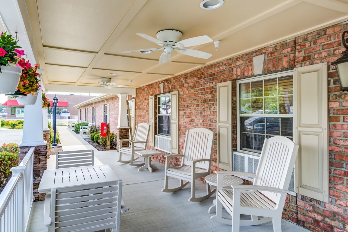 A cozy porch area with comfortable chairs and a ceiling fan under a covered patio.