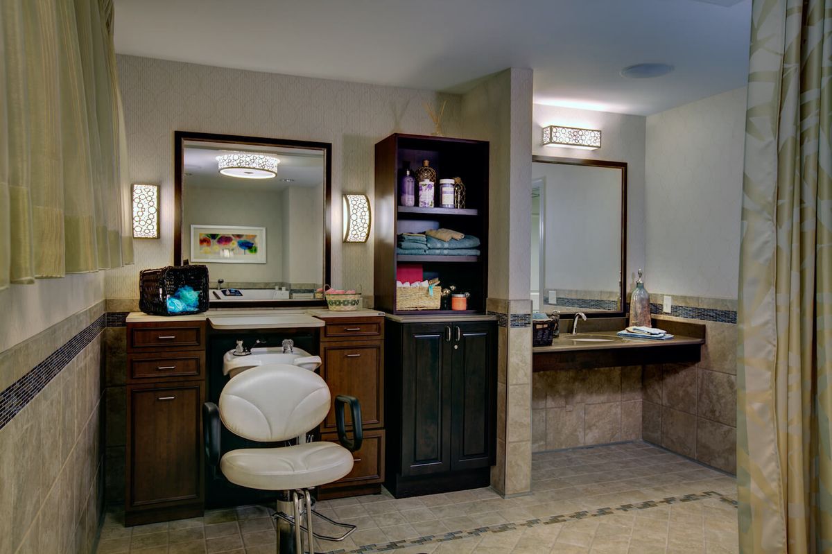 A modern bathroom vanity with mirrors, shelves, and a chair.