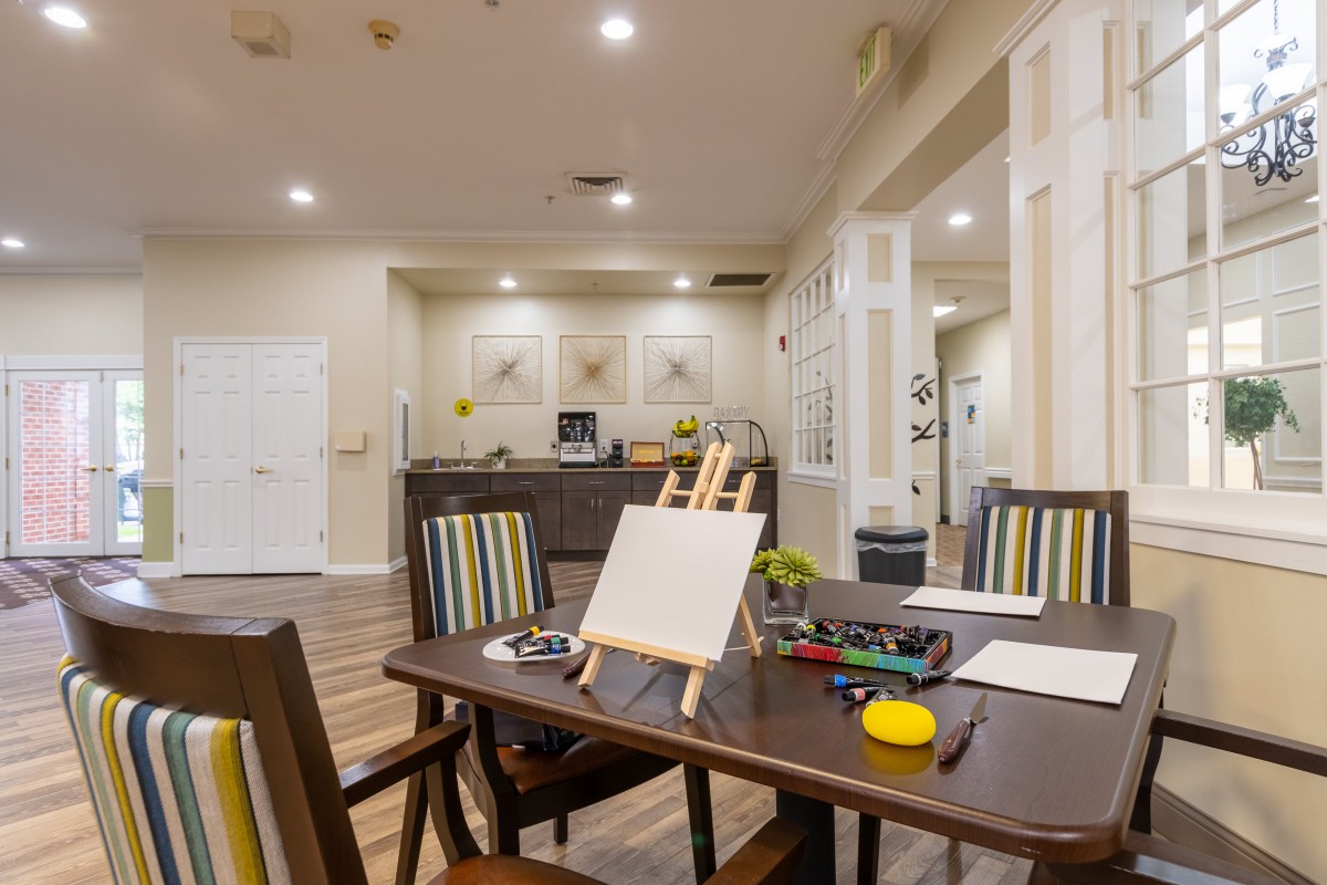 A well-lit art room with a table set for painting, featuring an easel and art supplies.