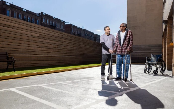 Two people are outdoors, one using crutches for support while the other provides assistance.