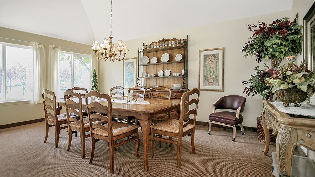 A traditional dining room with a wooden table and chairs, illuminated by a chandelier, features a china cabinet displaying decorative plates.