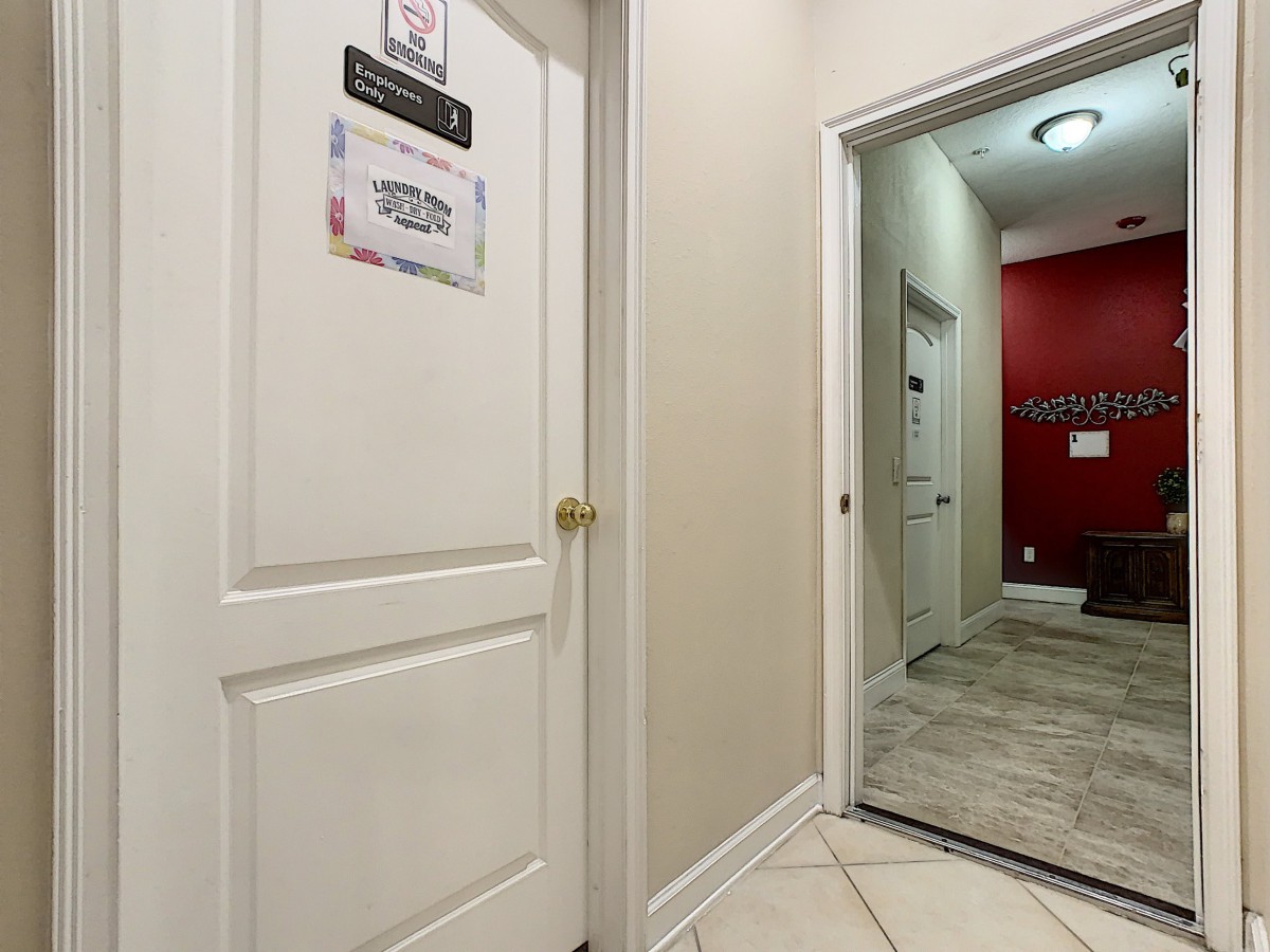 A view of a hallway featuring multiple doors, including a door with a sign, red accent walls, and tiled flooring.