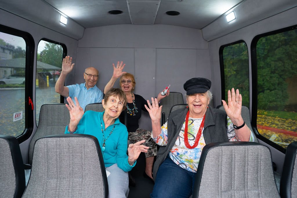 A cheerful group of seniors waving while sitting inside a bus.