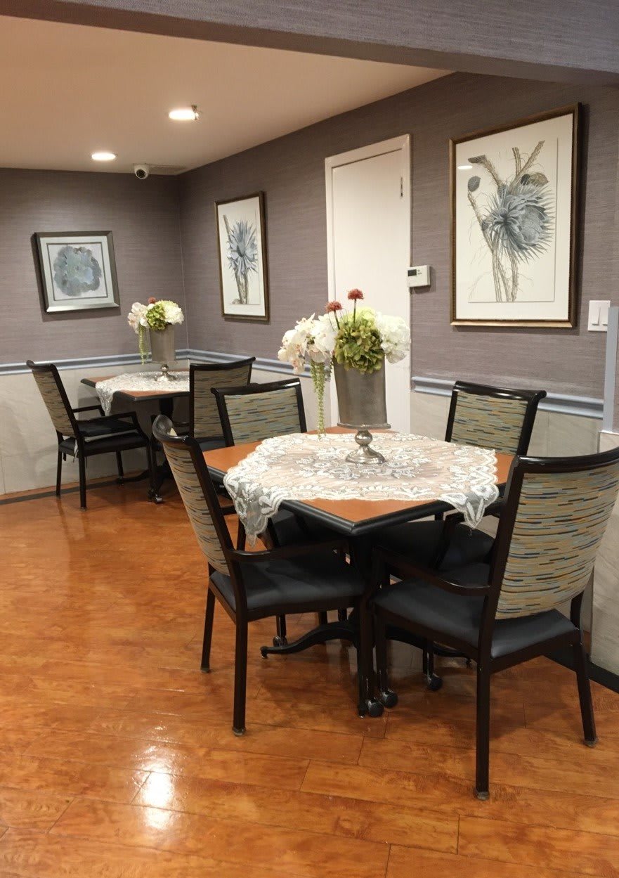 A cozy dining room with neatly arranged tables and chairs, adorned with floral decorations and framed artwork on the walls.