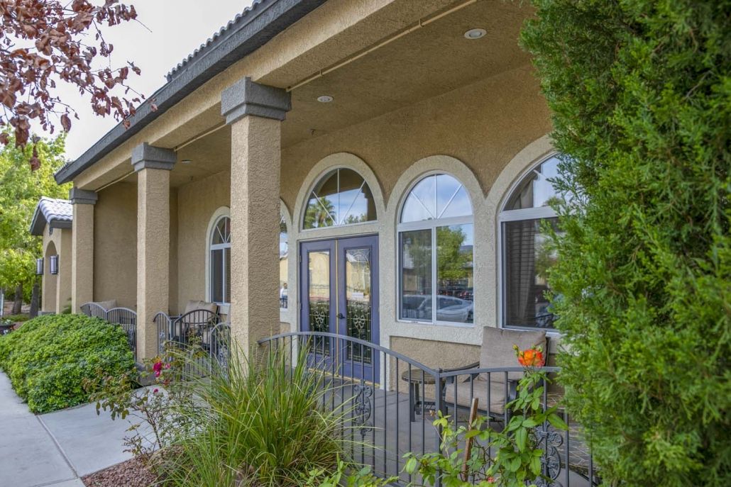 A view of a building entrance featuring arched windows, columns, and surrounding greenery.