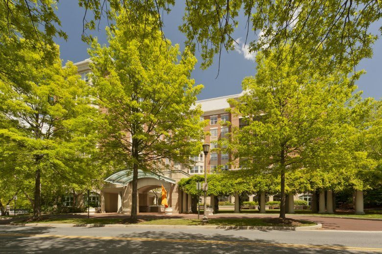 A building entrance surrounded by lush green trees under a clear blue sky.