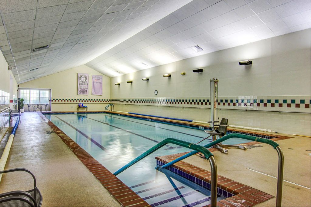 An empty indoor swimming pool with tiled walls and handrails.