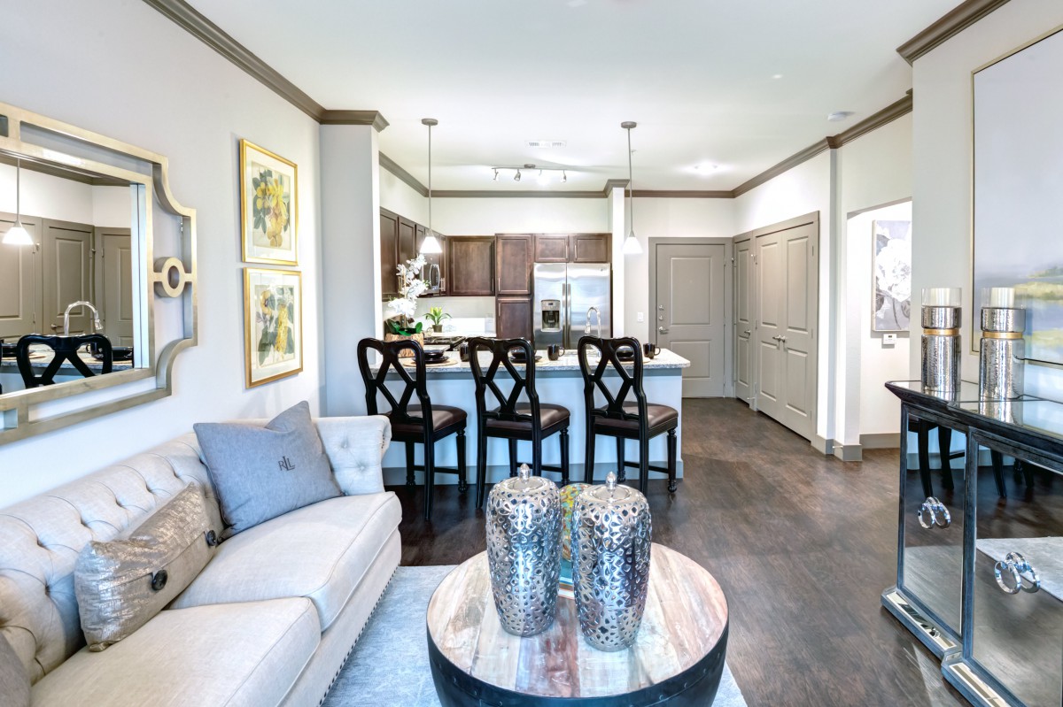 A modern living room with an open floor plan, featuring a kitchen area with bar stools and contemporary decor.