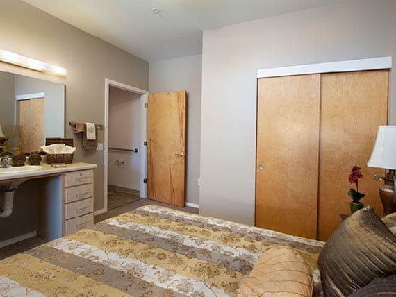 A cozy bedroom with a neatly made bed, wooden closet doors, and a small dresser.