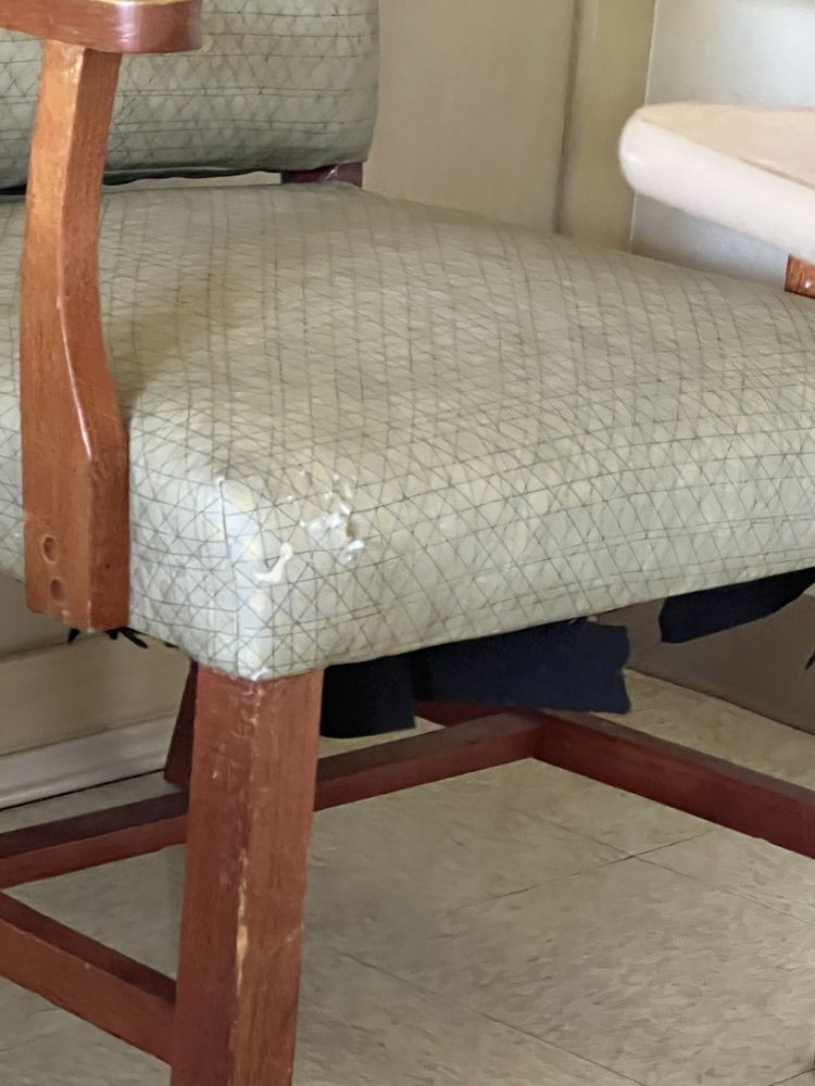 A close-up view of a chair with a wooden frame and worn upholstered fabric.