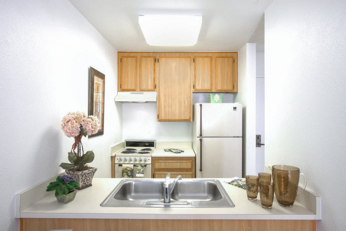 A clean and organized kitchen with wooden cabinets, a stainless steel refrigerator, and decorative elements on the countertop.