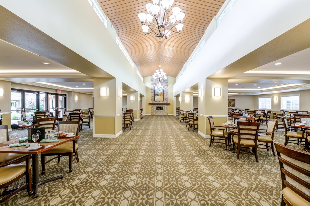 A spacious and elegantly designed dining hall with chandeliers, tables, and chairs arranged neatly on a patterned carpet.