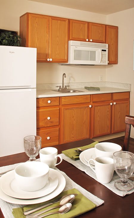 A cozy kitchen space featuring wooden cabinets, a microwave, and a refrigerator, with a dining table set for breakfast.