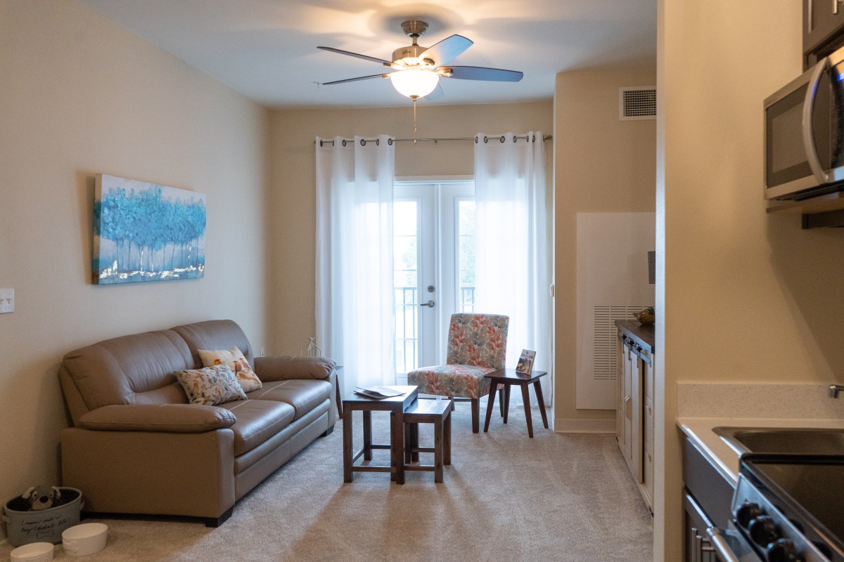 A cozy living room with a sofa, table, and chairs, featuring a ceiling fan and artwork on the wall.