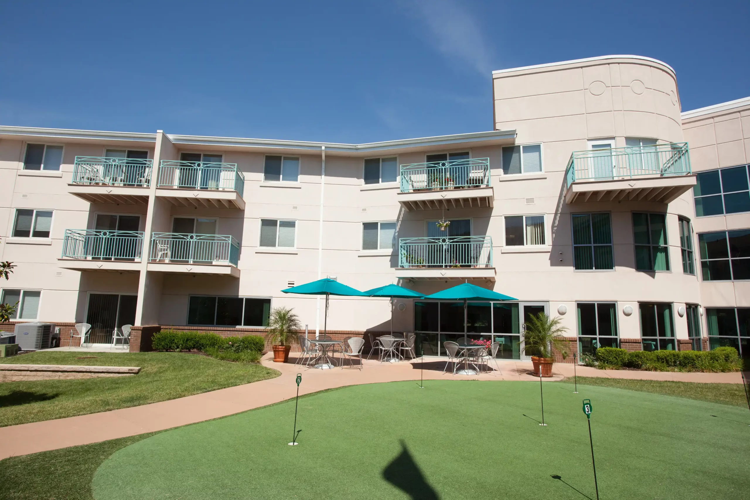 Modern apartment building with balconies and a putting green in the outdoor area.