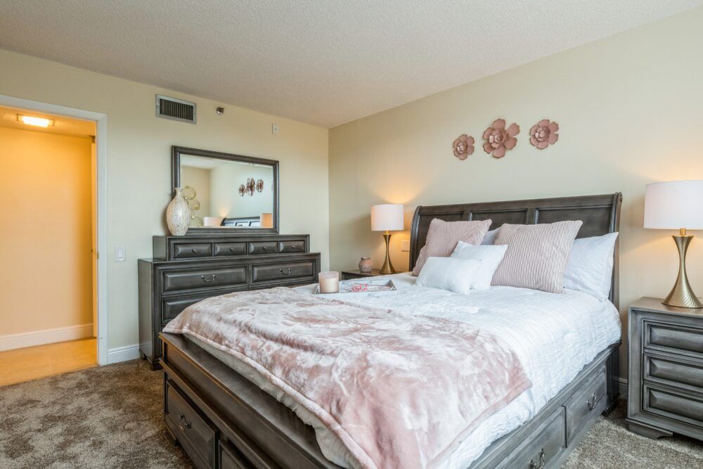 A cozy bedroom with a neatly made bed, decorative pillows, a bedside lamp, and a dresser with a mirror.