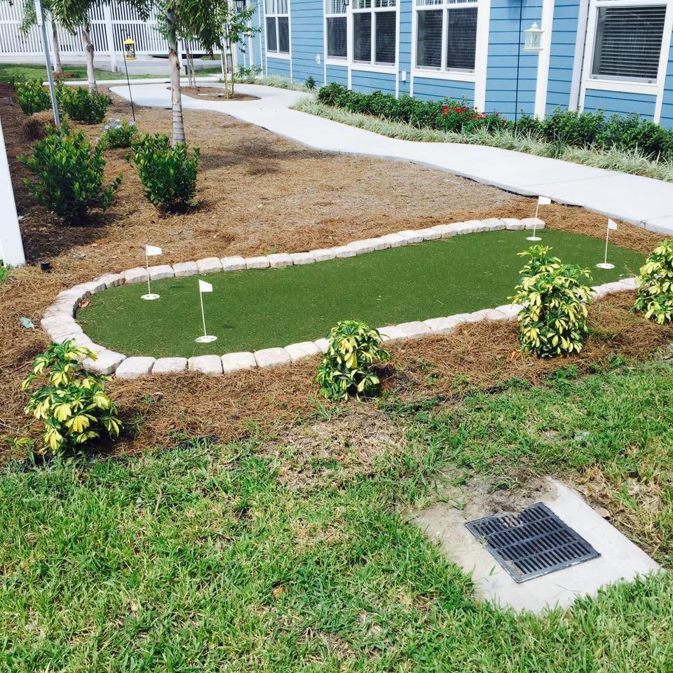 Outdoor mini golf putting green surrounded by landscaping.